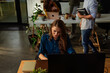 © bernardbodo - Focused employee working on computer in busy office with colleagues collaborating