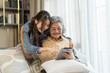 © Art_Photo - Asian senior mother and daughter smiling and talking using tablet browsing social media, shopping online, watching movies or series, enjoying entertainment digital connection and bonding at home