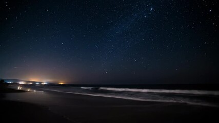 Wall Mural - stars slowly traverse the sky above an illuminated coastline as ocean waves gently crash on the shor