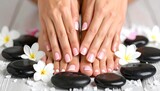 Pedicured feet and manicured hands rest amongst smooth black stones and white flowers, on a distressed wooden surface