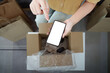 © Natee Meepian - Online shopping. Unboxing a delivery with smartphone in hand.
