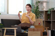 © Natee Meepian - Online Shopping. Happy woman showcasing credit card while sitting among shopping bags at home.