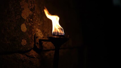 Sticker - timelapse of an ancient-looking torch burning brightly against a dark stone wall, fuel slowly consum