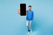 © ViDi Studio - Full body young man of African American ethnicity in sweatshirt casual clothes hold in hand use mobile cell phone with blank screen workspace area isolated on plain pastel light blue cyan background