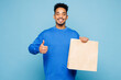 © ViDi Studio - Young man of African American ethnicity wear sweatshirt casual clothes hold brown clear blank craft paper takeaway bag mock up isolated on plain pastel light blue background studio. Lifestyle concept.