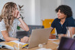 © Studio Marmellata - Two young people, a woman and a man, are having a discussion at a table. They are focused on their conversation, with a laptop and books nearby. This suggests a collaborative work or study session.
