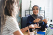 © Studio Marmellata - Two diverse women are engaged in a business meeting. The woman in a hijab listens intently while holding a pencil. They are collaborating in a modern office setting.