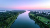 Scenic Aerial View of a City River at Dusk with Pink and Blue Sky Lush Green Trees and Distant Buildings in Golden Light
