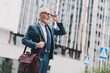 © deagreez - Successful senior businessman in formal suit walking outdoors with leather bag in urban city area