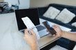 © Shi  - Close-up of man holding a receipt and smartphone while sitting at desk with laptop. Concept of online payment, personal finance, managing bills, e-banking, and household expenses.