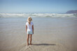 © wavebreak3 - Girl standing in wet sand at shoreline wearing straw sun hat and gazing at ocean waves