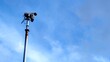 © Adrenaloby - A modern CCTV security camera on a tall pole against a bright blue sky, a concept of public safety and monitoring