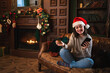 © Юлия Завалишина - Merry Christmas. Young woman shopping online holding smartphone paying with gold credit card for Christmas gifts. Girl buying on Internet enter credit card details enjoying winter holidays at home