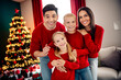 © deagreez - Family celebration in cozy home with festive Christmas tree, wearing matching red sweaters and sharing joyous holiday moments