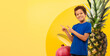 © Prostock-studio - A cheerful latin boy with curly hair smiles widely while pointing at copy space. He wears a blue t-shirt and stands against a vibrant yellow background with colorful fruit elements.