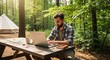 © ViskBx - Man working on laptop at picnic table in forest with tent in background on a sunny day outdoors scene