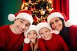 © deagreez - Smiling family celebrating Christmas together at home with festive decorations, wearing matching red sweaters and Santa hats