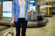 © Wavebreak Media - Woman in business casual standing at baggage carousel pulling suitcase and using smartphone