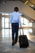 © Wavebreak Media - Man walking across marble lobby pulling black wheeled suitcase toward double glass doors
