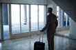 © Wavebreak Media - African American man standing beside glass doors in lobby holding rolling suitcase, copy space