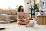 Sporty African-American woman with air humidifier and laptop meditating at home