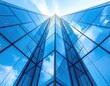 © bilbik - Vertically-angled view showcases a tall, modern glass skyscraper mirroring the blue sky and white clouds, emphasizing upward motion