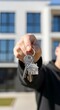© Shofia - A hand holding house keys, showcasing new homeownership in front of a modern building.