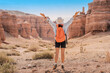 © EdNurg - Woman with orange backpack and white hat raising arms enjoying the view of Charyn Canyon in Kazakhstan