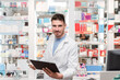 © Renata Hamuda - Male Pharmacist holding medication and using digital tablet in pharmacy looking at camera