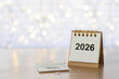 © Pcess609 - Desk calendar turning from 2025 to 2026 on a wooden table with warm bokeh lights, symbolizing year-end farewell, New Year celebration, resolutions, goals, and fresh beginnings with generous copy space