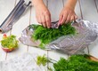 © Natallya_ph - Step-by-step preparation of frozen dill in a foil wrapper for freezer storage on a light wooden background.