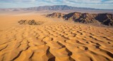 Aerial view of sand dunes in the desert with mountains in the background
