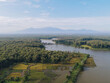 Aerial view of a patchwork of golden rice paddies meeting the dark waters, fringed by dense green forests under a hazy sky, [Actual City Name], [Actual State Name], [Actual Country Name].