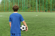 © Mediaphotos - Boy standing on outdoor soccer field holding soccer ball facing away from camera preparing for game