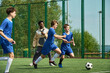 © Mediaphotos - Group of teenage boys running and competing for soccer ball on outdoor field while Black male coach observing and instructing during training session