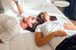 © simona - Happy young couple lying on bed during daytime, dressed in casual loungewear, smiling and talking. Dreaming together, sharing plans, enjoying love, a healthy relationship, and future aspirations