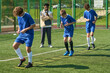 © Mediaphotos - Three teenage boys performing agility ladder drills on outdoor sports field while Black man coach observing and instructing in background during soccer training session