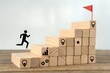 © Muhammad - Silhouette of person running up wooden block stairs towards a red flag at the top