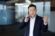 © Tetiana - Portrait of angry young Asian businessman standing in office and talking on phone emotionally