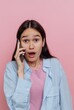 © bodnarphoto - Surprised woman talking on smartphone against pink background.