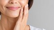 © Netsai - Close-up of a smiling mature woman's face, highlighting fine lines, as her hand gently touches her cheek against a neutral background.