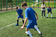 © Mediaphotos - Teenage boys playing soccer on outdoor field, one dribbling ball while another defending, two teenage boys including Black teenager standing on sideline watching action closely