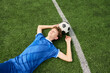 © Mediaphotos - Teenage boy lying on grass soccer field resting with soccer ball under head eyes closed hands behind head wearing sports uniform relaxing after match