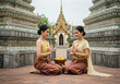© LSH - 2 young and pretty Thailand women in traditional costume with Thai greeting gesture, both sitting sideway on the floor in Thailand buddhist temple.