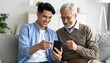 © Kim de Been - Young man and his elderly father looking at a mobile phone together. Two generations using technology