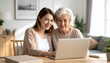 © Kim de Been - Elderly mother and daughter sitting at a desk, looking at a laptop. Two generations using technology together