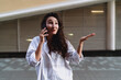 © BullRun - Young woman in oversized shirt holding smartphone to ear, expressing emotions during conversation. Conceptual photo symbolizing digital communication, connection, and expressive interaction.