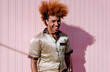 © BullRun - Stylish young African American man with curly ginger hair smiling naturally, leaning toward camera, bathed in warm sunlight, blending fashion-forward elegance with relaxed urban vibe.