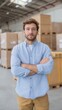 © Pro Hi-Res - Logistics employee standing confidently in a warehouse surrounded by stacked boxes in a busy distribution center.