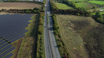 Aerial drone footage of busy highway motorway road with traffic and solar panels, photovoltaic energy generation electricity sunlight near Leicester, United Kingdom